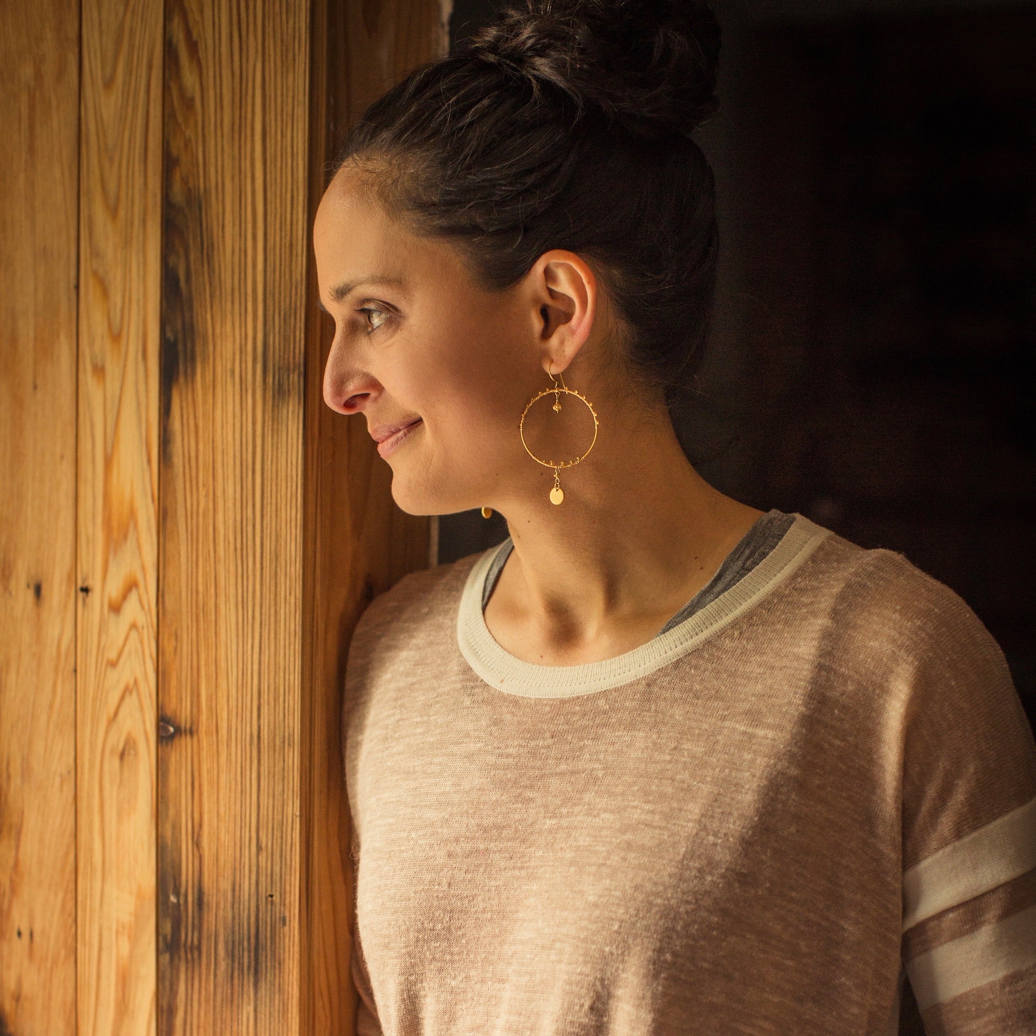 Woman in natural light wearing Sara Silvio gold earrings against a warm wood background — Virtual Color Analysis with Sara Silvio